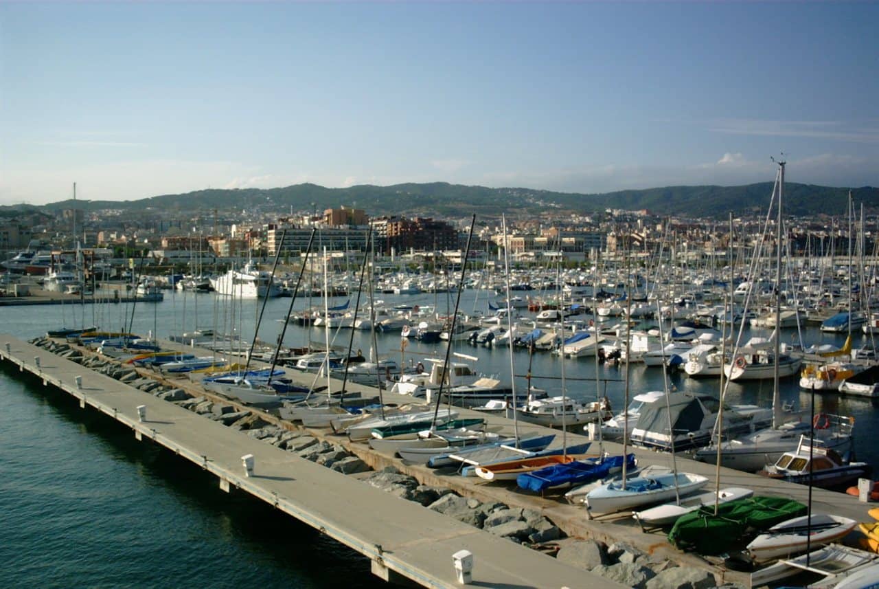 Yates y veleros amarrados en el puerto de Mataró, con colinas detrás de la ciudad
