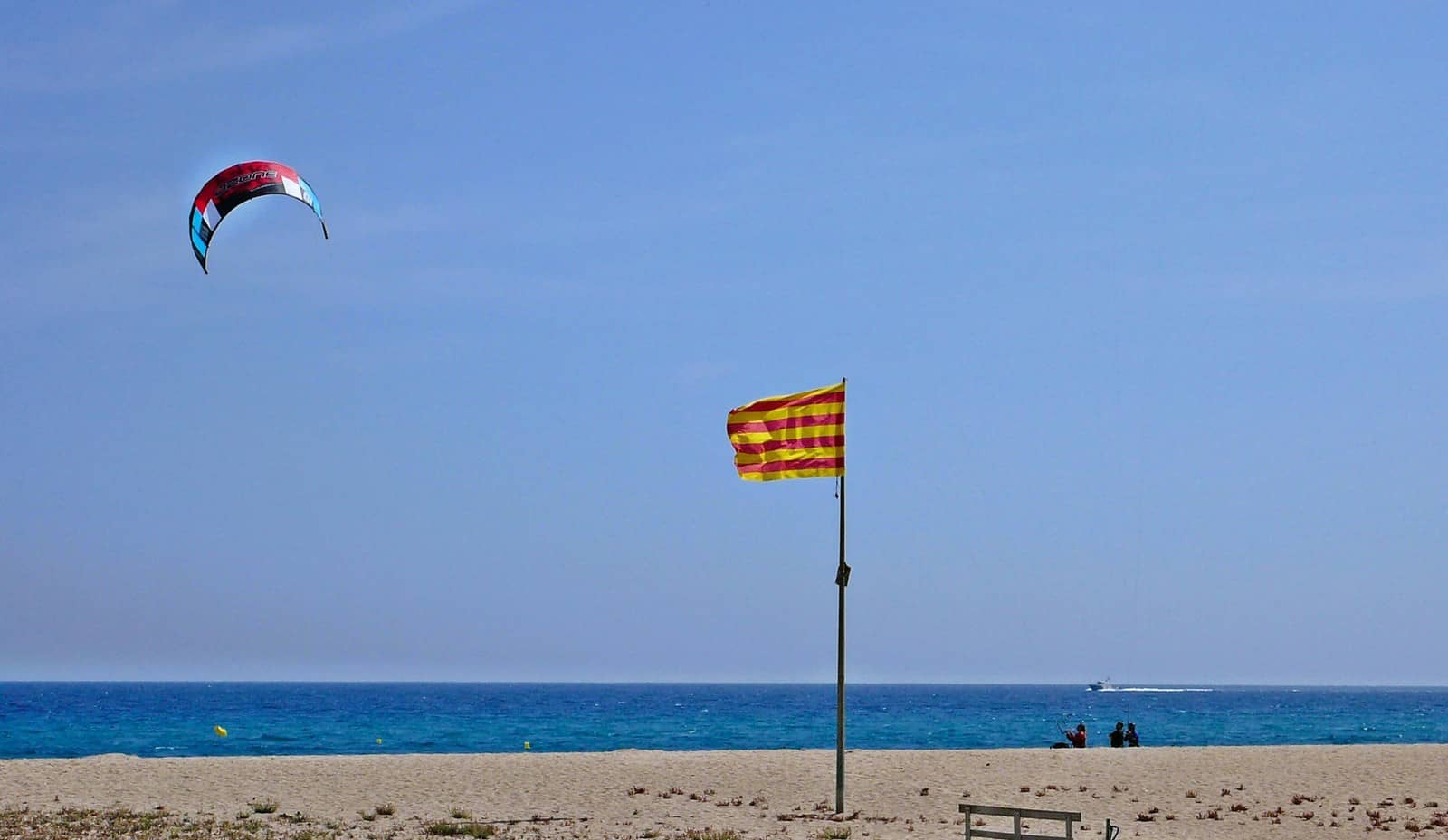 La amplia playa de Malgrat de Mar: la bandera de Cataluña y una cometa de kitesurf sobre el mar