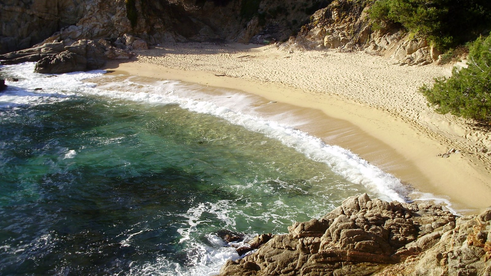 A small Costa Brava cove from above: turquoise water, a strip of sand and rocks on either side