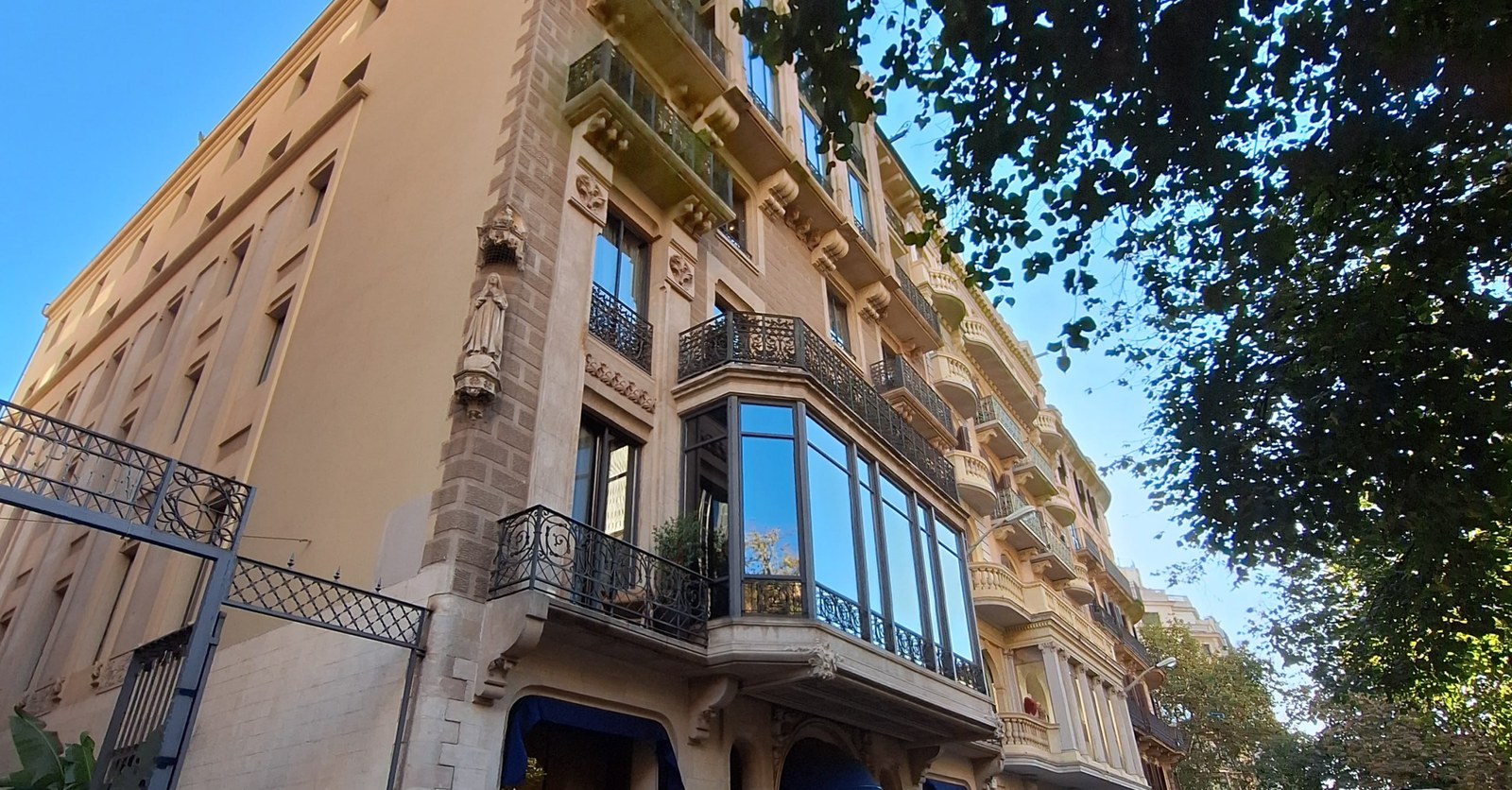 Edifici de cantonada a la Rambla de Catalunya: sòcol de pedra, una escultura a la fornícula i tribunes envidrades