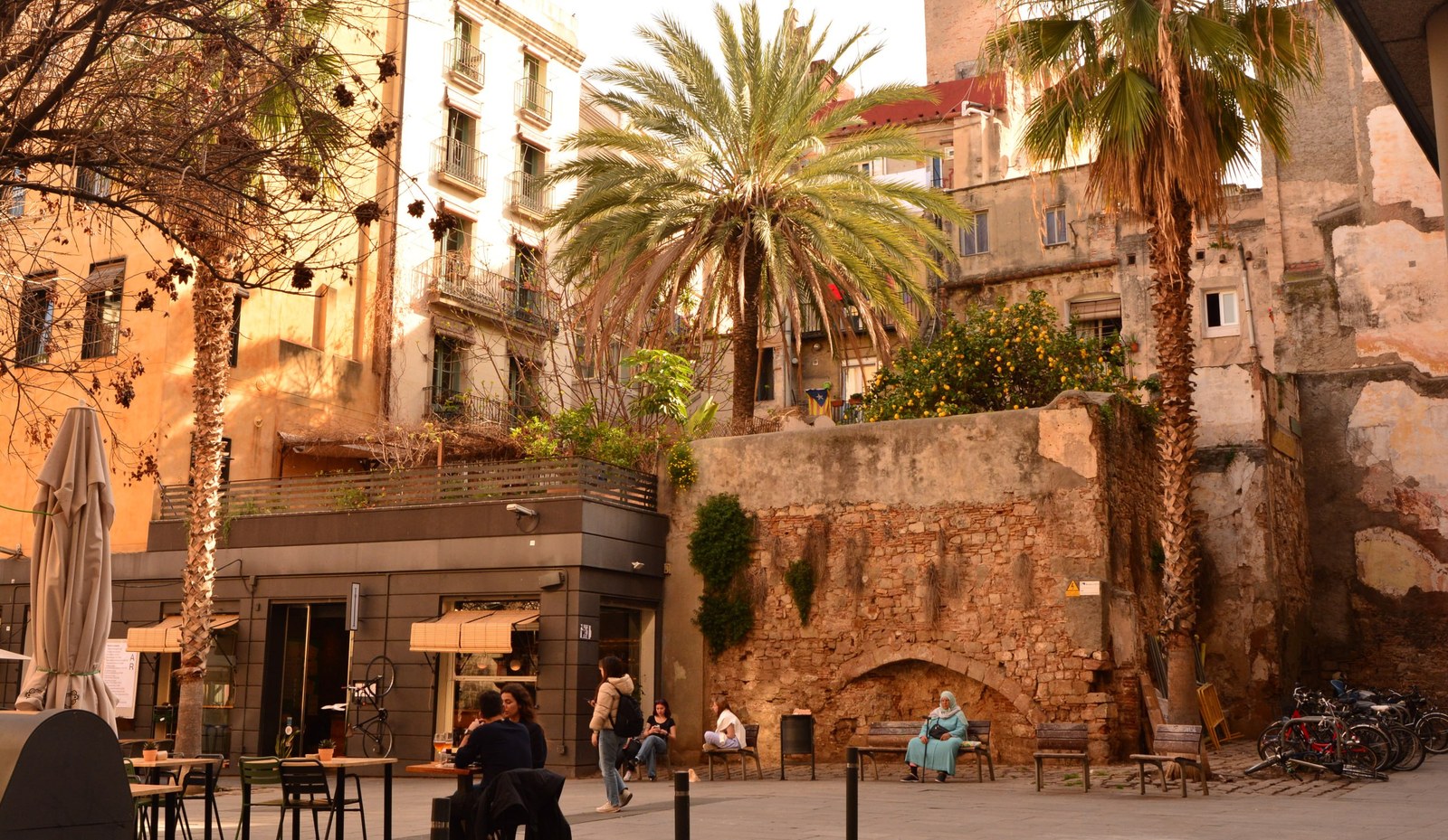 Plaça del nucli antic de Sant Cugat: cafès, palmeres i un vell mur de pedra