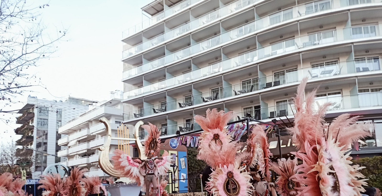 Sitges Carnival: a float with feathered dancers by the facade of Hotel Calipolis