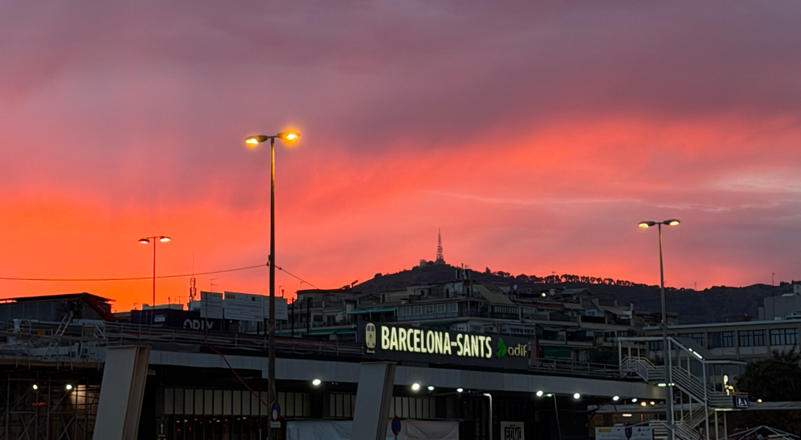 Schild des Bahnhofs Barcelona Sants bei Sonnenuntergang, dahinter der Tibidabo mit dem Fernsehturm