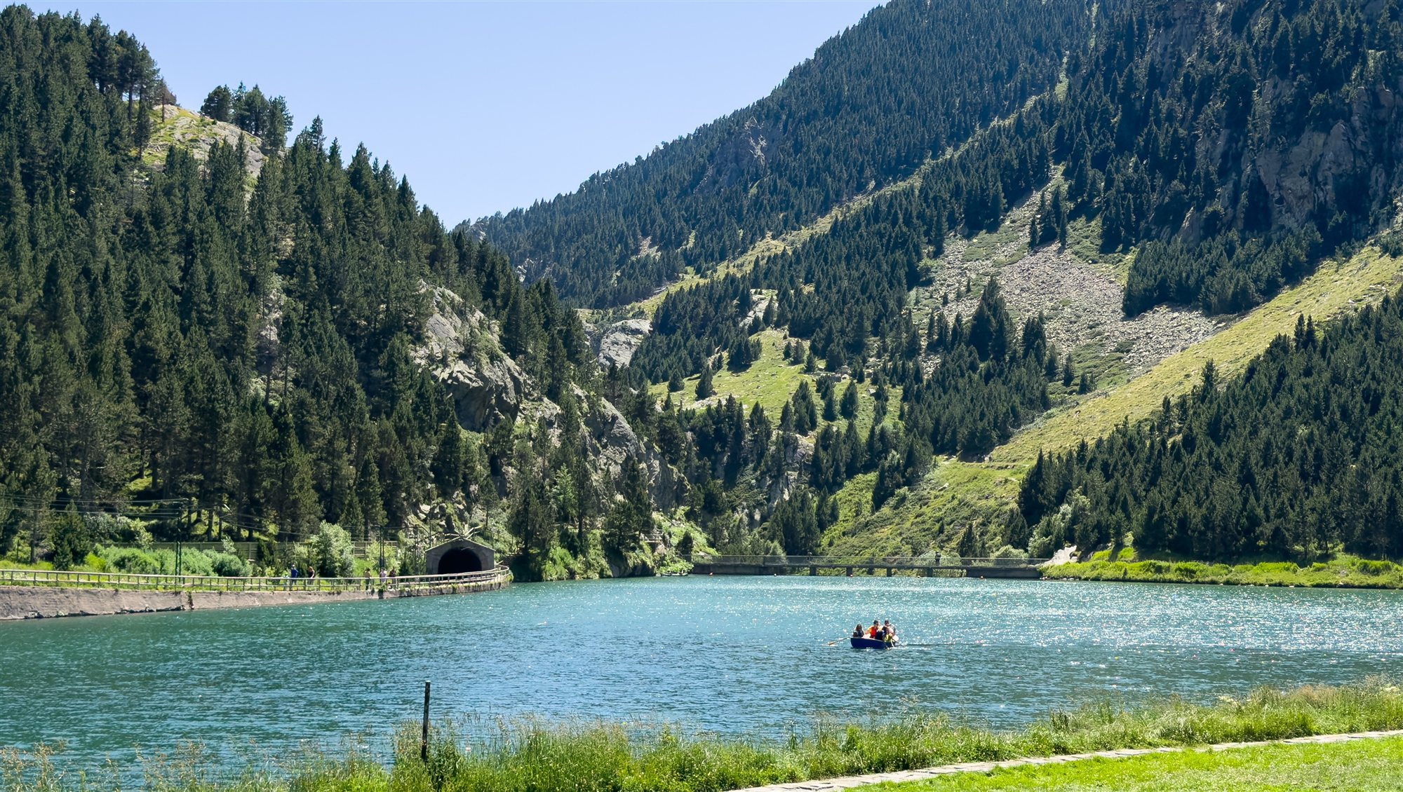 Bergsee im Tal von Núria im Sommer, am Ufer der Tunneleingang der Zahnradbahn