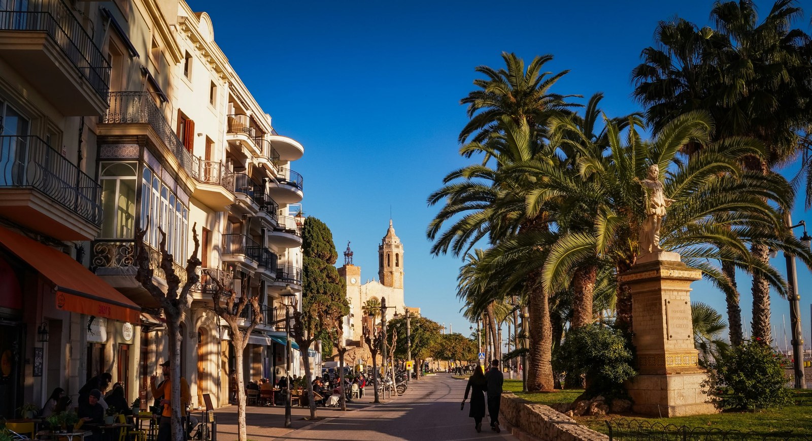 The Sitges seafront with palm trees and Sant Bartomeu church in the distance