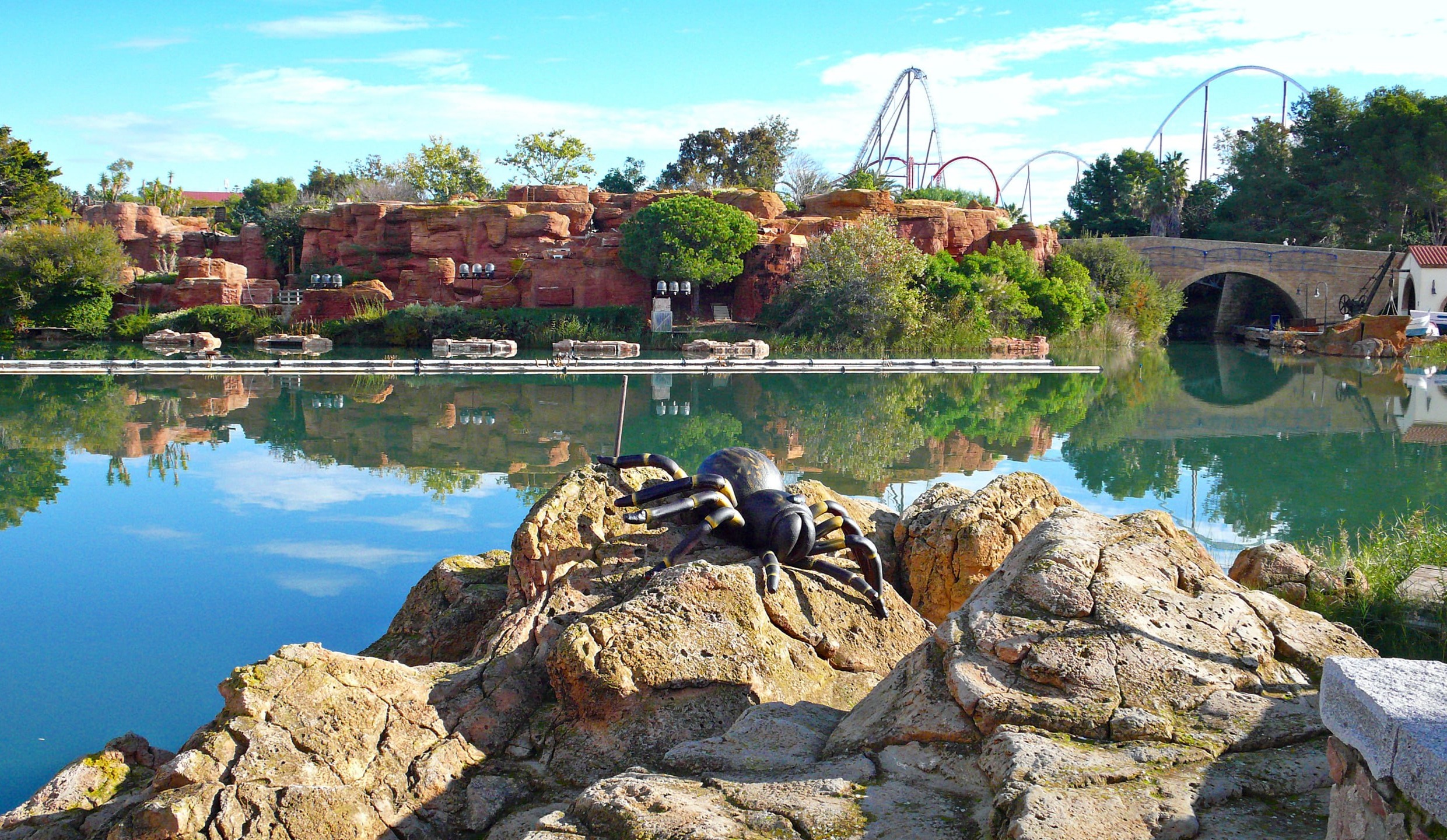 Llac i roques a la zona temàtica de PortAventura, la muntanya russa a l'horitzó