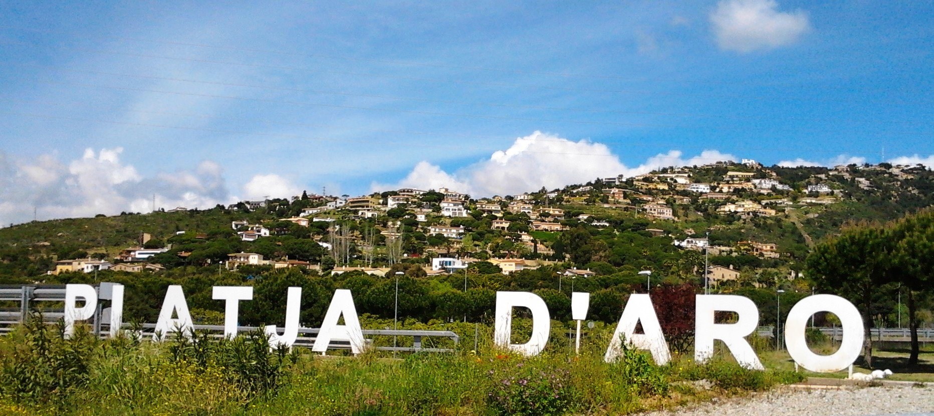 Les lletres blanques de PLATJA D'ARO a l'entrada del poble, amb el turó de les vil·les al darrere