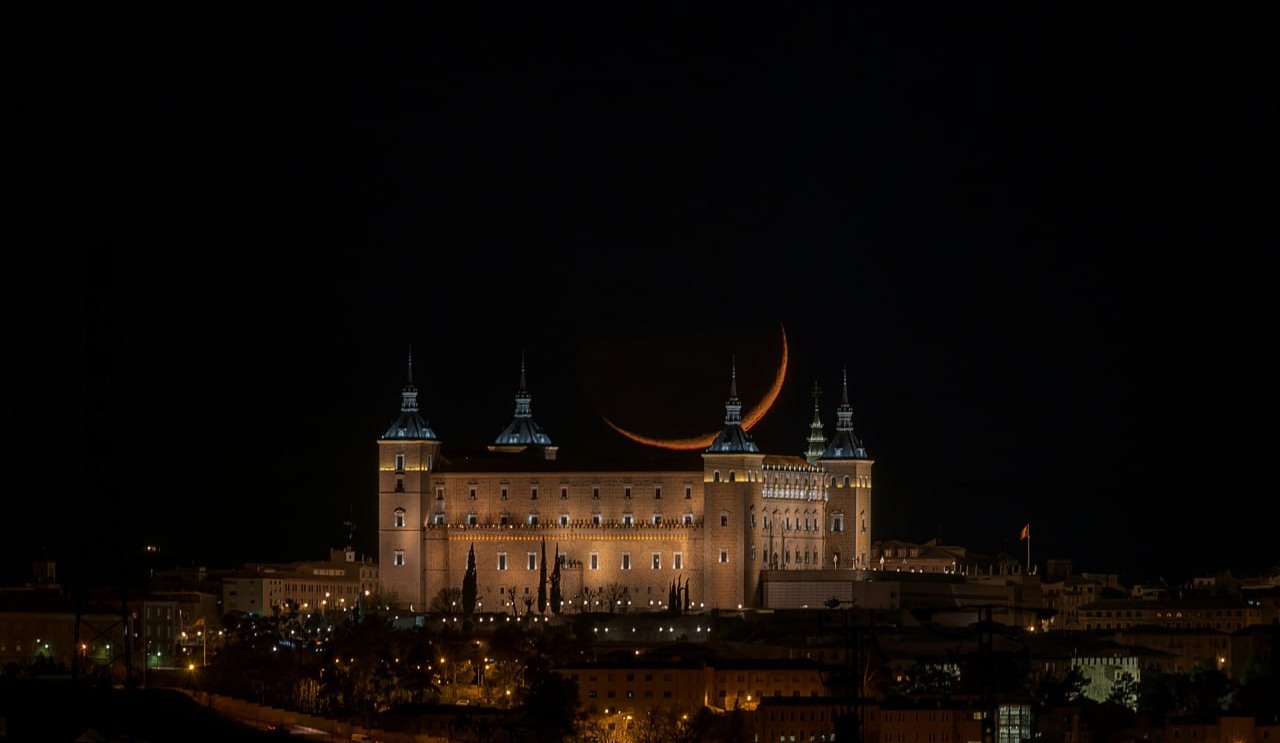 Der beleuchtete Alcázar von Toledo bei Nacht, dahinter die Mondsichel