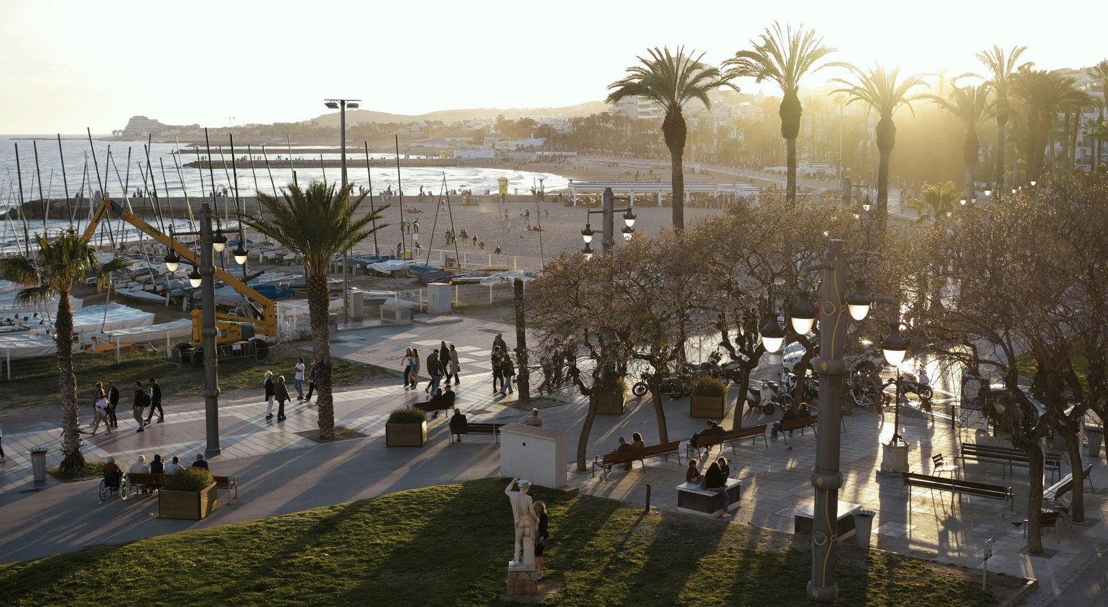El passeig marítim de Sitges al capvespre: palmeres, velers sobre la sorra i la platja